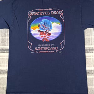 May include: Navy blue t-shirt featuring a graphic of a blue rose with the words "Grateful Dead" and "The Closing of Winterland December 31, 1978". The design is set within an oval frame.