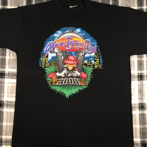 May include: Black t-shirt with a graphic of a mushroom and the text "The Allman Brothers Band 2000" in a city skyline setting.