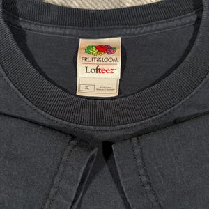 May include: A solid dark navy blue t-shirt with a ribbed crew neckline. The interior neck label features the Fruit of the Loom logo, the text Lofteez, and a size XL tag indicating 100% cotton construction, with the origin marked as El Salvador.
