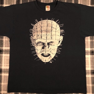 May include: Black t-shirt with a white graphic print of a character from the horror movie "Hellraiser". The character has a head covered in nails and a grid pattern.