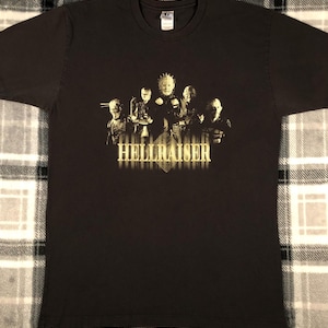 May include: Black t-shirt with a gold graphic of the characters from the horror film Hellraiser. The graphic features the Cenobites, including Pinhead, with the title "Hellraiser" printed below.