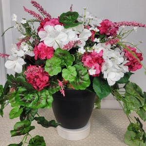 May include: A vibrant floral arrangement featuring white, pink, and fuchsia flowers, accented by green leaves and delicate pink sprigs. The flowers are arranged in a black pot, creating a striking contrast. A decorative piece for home decor.