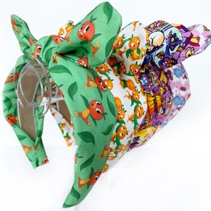 May include: A green headband with a bow featuring a cartoon orange bird print. The headband is made of fabric and has a plastic base.