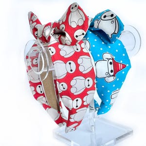 May include: Two fabric headbands with a bow. One headband is red with white cartoon robots, the other is blue with white cartoon robots.