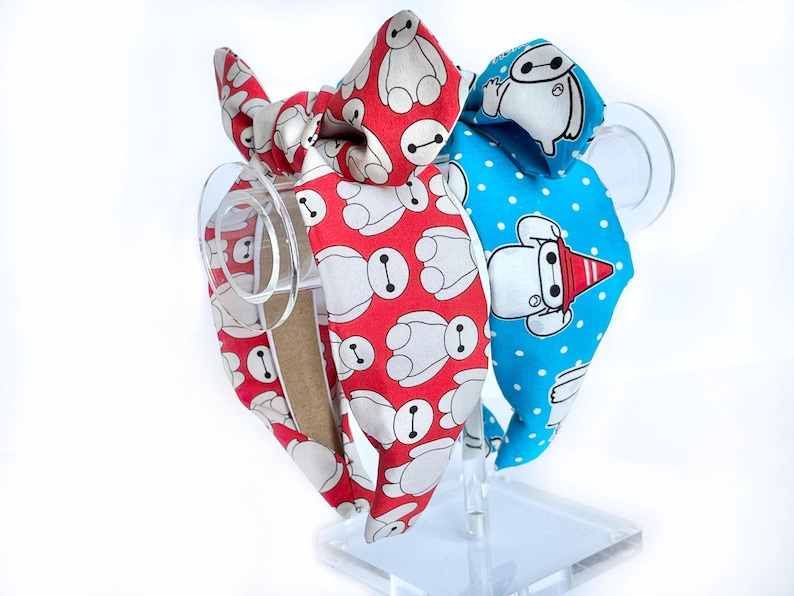 May include: Two fabric headbands with a bow. One headband is red with white cartoon robots, the other is blue with white cartoon robots.