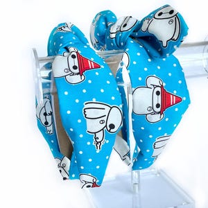 May include: Two blue headbands with white polka dots and a cartoon character design. The character is white with red accents and is wearing a red hat.