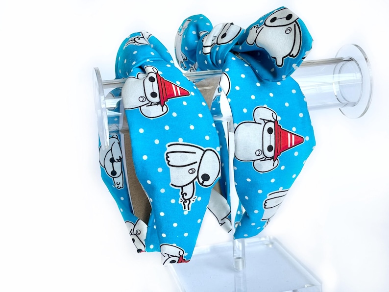 May include: Two blue headbands with white polka dots and a cartoon character design. The character is white with red accents and is wearing a red hat.