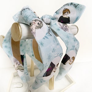 May include: Three blue headbands with a white background and a snowflake pattern. The headbands feature images of the characters from the movie Frozen, including Elsa and Anna. The text "Let it go" and "Follow your heart" are printed on the headbands.