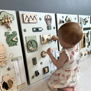 May include: A set of three sensory boards with various wooden elements for toddlers. Features include a clock, gears, zippers, latches, and a shoe with laces. The boards are in neutral tones with green and beige accents, designed for early childhood development.