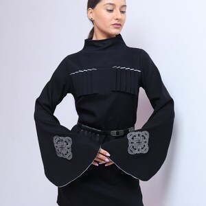 Puede incluir: Un vestido negro con mangas largas y un ribete blanco. Las mangas tienen un dise&ntilde;o bordado blanco. El vestido tiene un cintur&oacute;n negro.