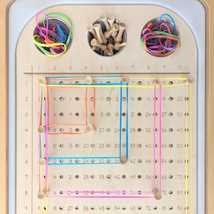 May include: A wooden board with a grid of 100 holes, numbered 1 to 100.  Four different colored rubber bands are stretched across the board, creating a square shape.  The board is designed for a children's educational toy.