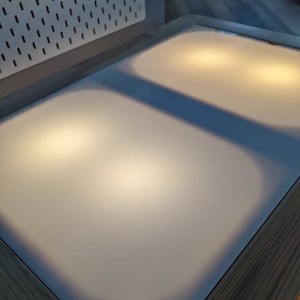 May include: A white rectangular surface with two light sources, creating a soft glow. The surface is framed by a dark wood border.