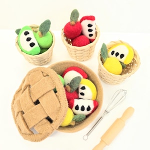 May include: A felted apple pie set with a pie crust, baskets of apples, and a rolling pin. The apples are red, green, and yellow, with green leaves and black seeds. The pie crust is tan, and the rolling pin is light brown.