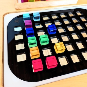 Może przedstawiać: Czarna siatka z kolorowymi, przezroczystymi blokami w różnych kolorach, w tym czerwony, pomarańczowy, żółty, zielony, niebieski i fioletowy. Bloki są ułożone w wzór na siatce.