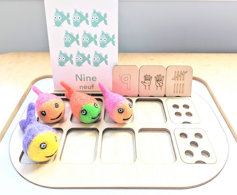 May include: A wooden learning tray with nine felt fish, a card with the word "Nine" and the French word "neuf", and wooden blocks with the number 9, a hand with five fingers, and tally marks.