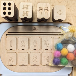 May include: Wooden counting tray with a set of number tiles, tally marks, and hand shapes. A bag of colorful felt balls is included.