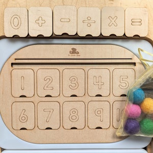 May include: Wooden toy with a number board and a set of colorful felt balls. The board has numbers 0-10 and symbols for addition, subtraction, division, multiplication, and equals. The felt balls are in a mesh bag.