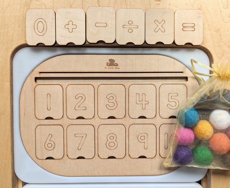 May include: Wooden toy with a number board and a set of colorful felt balls. The board has numbers 0-10 and symbols for addition, subtraction, division, multiplication, and equals. The felt balls are in a mesh bag.