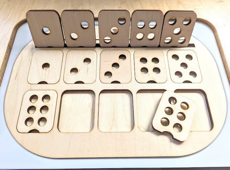 May include: A wooden game board with nine compartments, each containing a different number of holes. The board is made of light wood and has a rounded edge. There are also five separate wooden pieces with different numbers of holes.