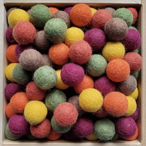 Peut inclure: Une collection de nombreuses petites boules en feutre rondes de diverses couleurs, notamment orange, jaune, vert, violet et marron, serrées dans un cadre en bois carré. Les sphères présentent une surface texturée et duveteuse.