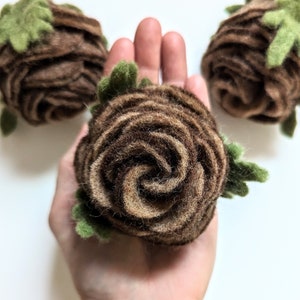 May include: Three brown and green felt roses. The roses are hand-crafted and have a spiral design. The roses are on a white background.