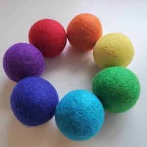 Peut inclure: Huit boules de feutre de couleurs vives disposées en cercle : rouge, orange, jaune, vert, bleu, turquoise et violet. Les boules sont espacées uniformément et semblent faites à la main.