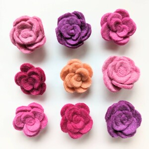 May include: Nine felt flower embellishments in various shades of pink, purple, and orange. The flowers are all the same size and shape, with a simple, rounded design.