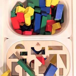 May include: A wooden toy with a cutout shape sorting board and a separate container filled with colorful wooden blocks. The board has a variety of shapes cut out, including circles, squares, triangles, and rectangles. The blocks are red, blue, green, and yellow.