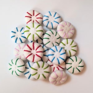 May include: A collection of felt peppermint sweets in various colours, including red, green, blue, pink, and white. The sweets are arranged in a pile on a white background.