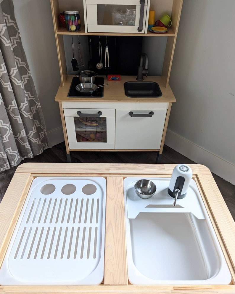 Puede incluir: Un juego de cocina de madera para ni&ntilde;os con un fregadero blanco, un escurridor blanco y un dispensador de jab&oacute;n blanco. El juego de cocina est&aacute; hecho de madera y tiene un acabado natural. El fregadero est&aacute; hecho de pl&aacute;stico y tiene un acabado blanco. El escurridor est&aacute; hecho de pl&aacute;stico y tiene un acabado blanco. El dispensador de jab&oacute;n est&aacute; hecho de pl&aacute;stico y tiene un acabado blanco.