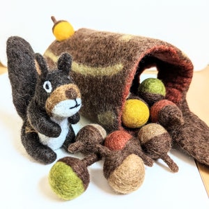 Könnte beinhalten: Ein brauner Filzstamm mit einem Eichhörnchen und Eicheln. Der Stamm ist offen und mit Filzeicheln in verschiedenen Farben gefüllt, darunter Gelb, Grün und Braun.