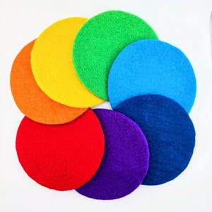 Può includere: Una composizione di cerchi di feltro colorati nei colori dell'arcobaleno: rosso, arancione, giallo, verde, blu, indaco e viola. I cerchi sono disposti a cerchio. Il feltro ha un aspetto morbido e strutturato.