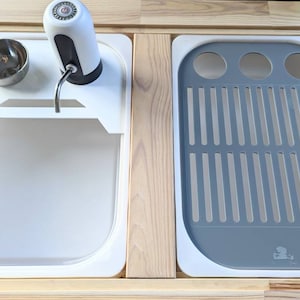 Puede incluir: Un fregadero de encimera blanco con un dispensador de jab&oacute;n incorporado y un escurridor de platos gris. El fregadero est&aacute; hecho de un material duradero y es perfecto para cocinas peque&ntilde;as o autocaravanas.