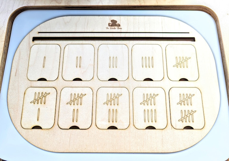 May include: A wooden counting tray with ten compartments, each containing a different number of tally marks. The tray is labeled "The Number Shop".