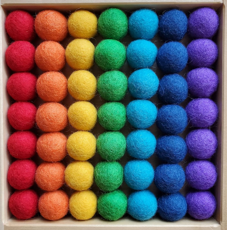 May include: A rainbow of felt balls arranged in a grid pattern. The balls are in shades of red, orange, yellow, green, blue, indigo, and violet.
