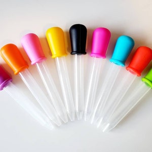 Puede incluir: Un conjunto de diez goteros de plástico de colores vivos con tubos de vidrio transparentes. Los goteros están dispuestos en semicírculo con las puntas apuntando hacia el centro.