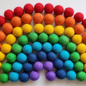 May include: A rainbow of felt balls arranged in a semi-circle shape. The balls are red, orange, yellow, green, blue, indigo, and violet.