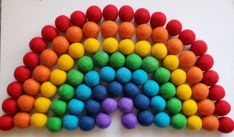 May include: A rainbow of felt balls arranged in a semi-circle shape. The balls are red, orange, yellow, green, blue, indigo, and violet.