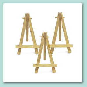 Könnte beinhalten: Drei kleine Holzstaffeleien, jede mit einem dreieckigen Rahmen und einer horizontalen Querstrebe. Die Staffeleien sind aus Naturholz gefertigt und eignen sich perfekt zum Ausstellen kleiner Kunstwerke oder Fotos.