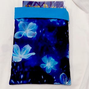 Peut inclure: Une housse à imprimé floral bleu et noir avec une bordure bleu vif. La housse présente de grands motifs de fleurs bleu clair. La housse semble contenir un objet rectangulaire.