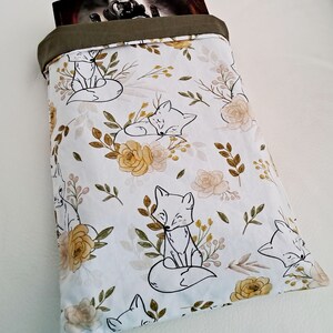 Peut inclure: Un sac en tissu blanc avec un dessus vert, orné d'un motif répétitif de renards et de fleurs. Le sac est rempli d'un livre.