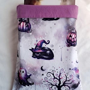 Peut inclure: Une housse de livre violette avec un fond blanc orné d'un motif répété de chats noirs, de citrouilles, de fantômes et d'un arbre effrayant. Le motif est réalisé dans un style aquarelle avec un fond de type galaxie.