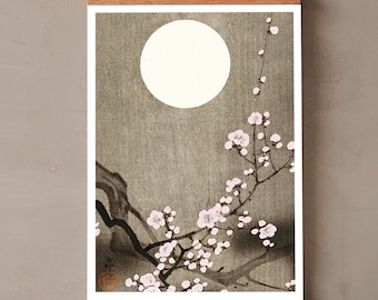 May include: A framed print of a Japanese-style painting depicting a blooming cherry blossom branch with a full moon in the background. The painting is done in shades of grey and pink.