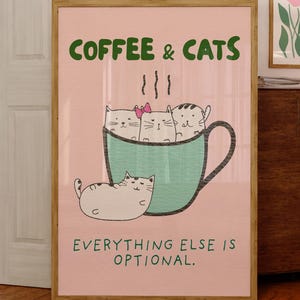 Könnte beinhalten: Ein gerahmter Kunstdruck mit den Worten "COFFEE & CATS" in Grün und "EVERYTHING ELSE IS OPTIONAL" in Schwarz. Das Kunstwerk zeigt eine türkisfarbene Kaffeetasse mit Cartoon-Katzen und eine Katze, die außerhalb der Tasse liegt.