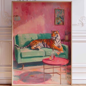 May include: A framed art print depicts a tiger lounging on a green sofa in a pink room. A small red table with drinks sits in front of the sofa. The tiger has orange and black stripes. The artwork is in a gold frame.