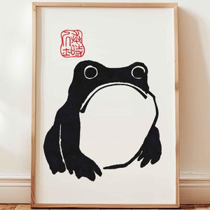 Peut inclure: Illustration en noir et blanc d'une grenouille avec un tampon de caractère japonais rouge au-dessus. La grenouille est face à l'avant, la bouche ouverte et les yeux fermés.
