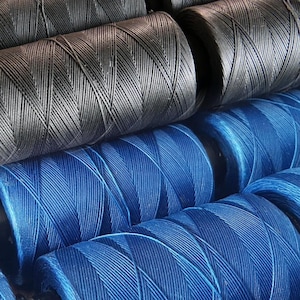 Op de afbeelding: Close-up van spoelen garen, sommige zijn zwart en sommige zijn blauw. Het garen is strak om de spoelen gewikkeld.