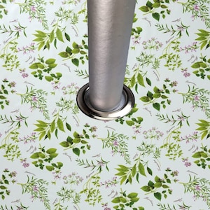 May include: A white surface adorned with a repeating pattern of green herbs and purple flowers. The design features basil, thyme, and oregano. A silver metal pole is centrally positioned, encircled by a silver metal ring.