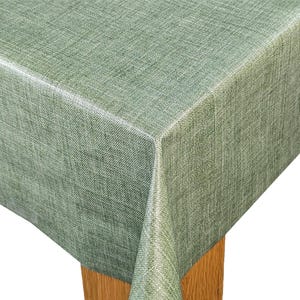 May include: A sage green tablecloth with a textured, linen-like appearance. The fabric drapes over the corner of a wooden table, showcasing the material's weave and colour variations. The tablecloth is suitable for dining and kitchen decor.