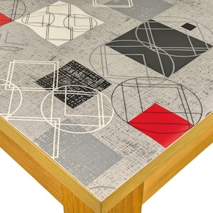May include: A grey and white table cover with a geometric pattern of black and red squares and circles. The table cover is made of a textured fabric.